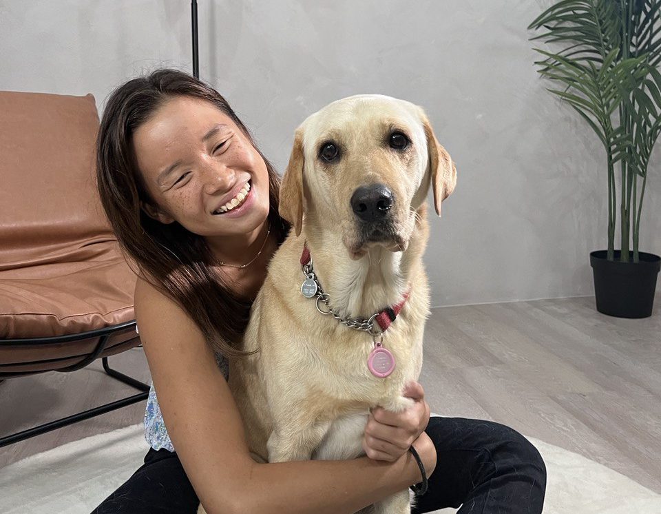 A guide dog user is sitting on the floor and hugging her yellow Labrador guide dog.