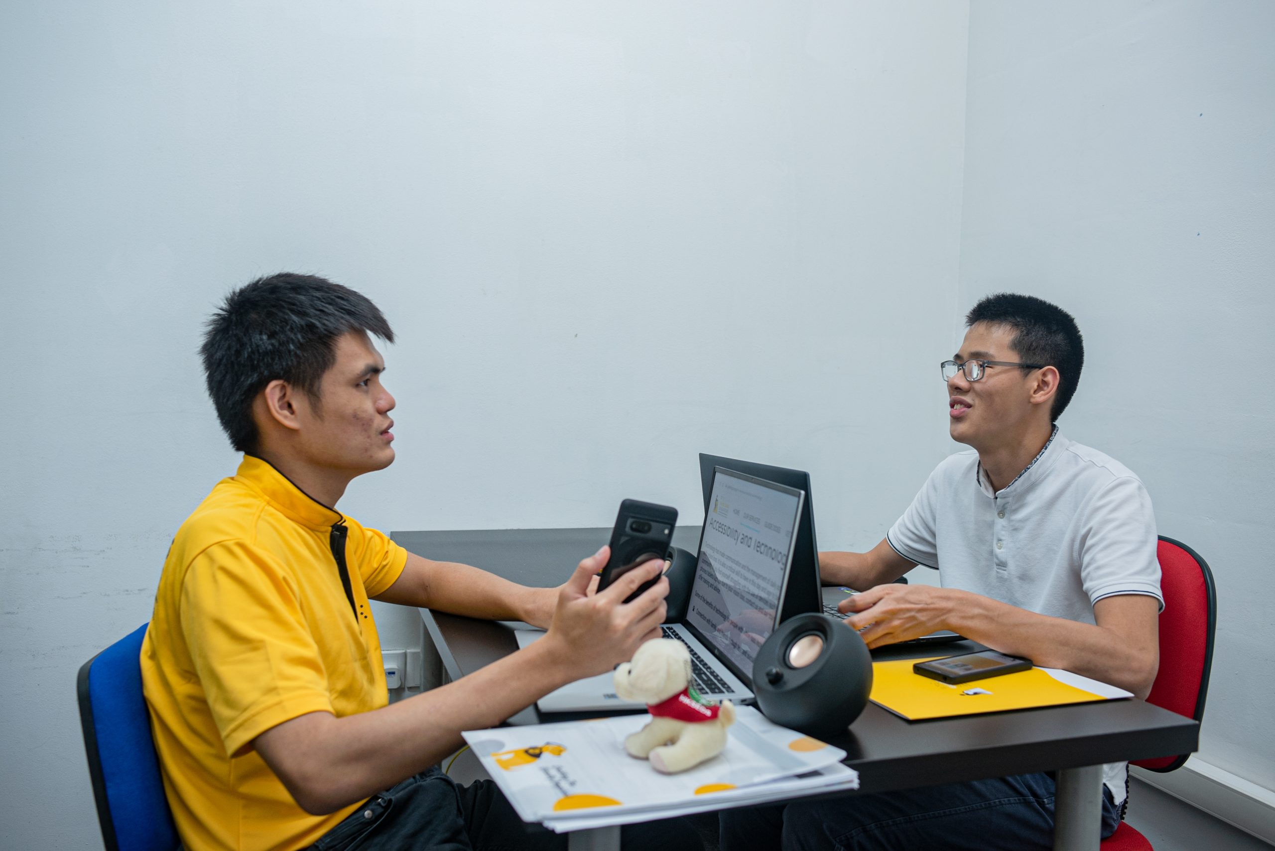 A side view of Hong Sen and Dallon sitting at the opposite side of the table and using their laptop respectively.