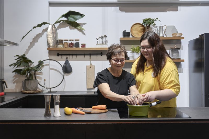 A GDS client and a staff member are cooking together in the kitchen, engaged in meal preparation.
