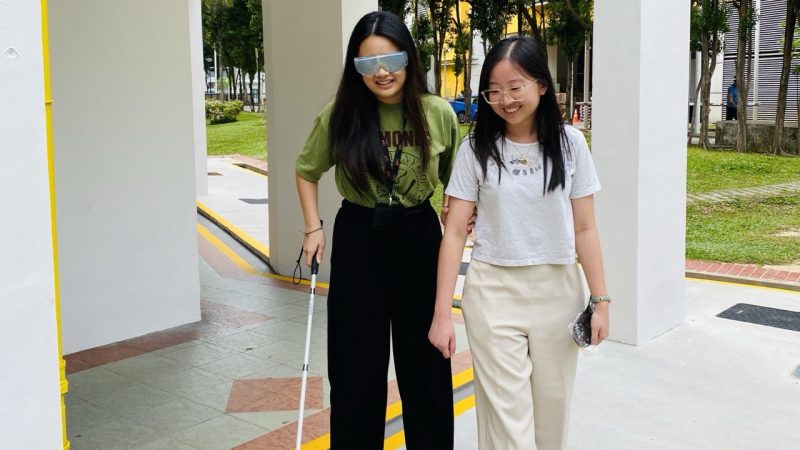 An educator wearing a blindfold and using a white cane, being guided by another educator for sighted assistance.