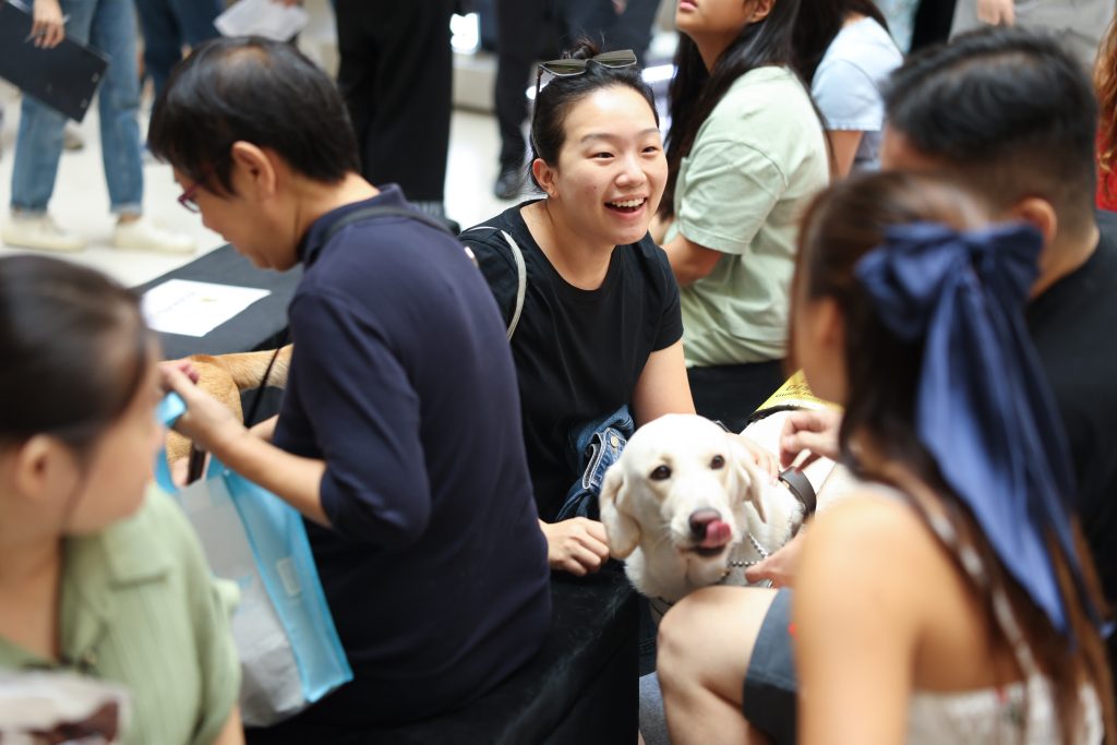 A volunteer appears to be talking with a guide dog user, as the user’s guide dog stands in front of them.