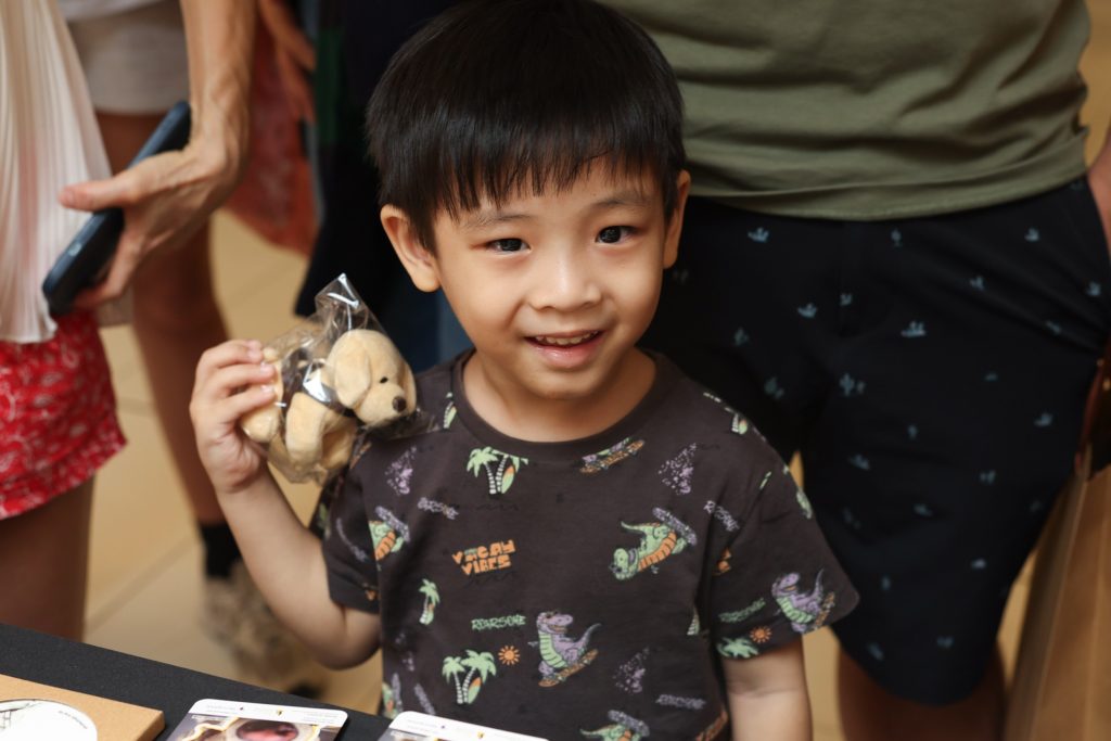 A young boy smiles while holding a beige guide dog plush keychain. 
