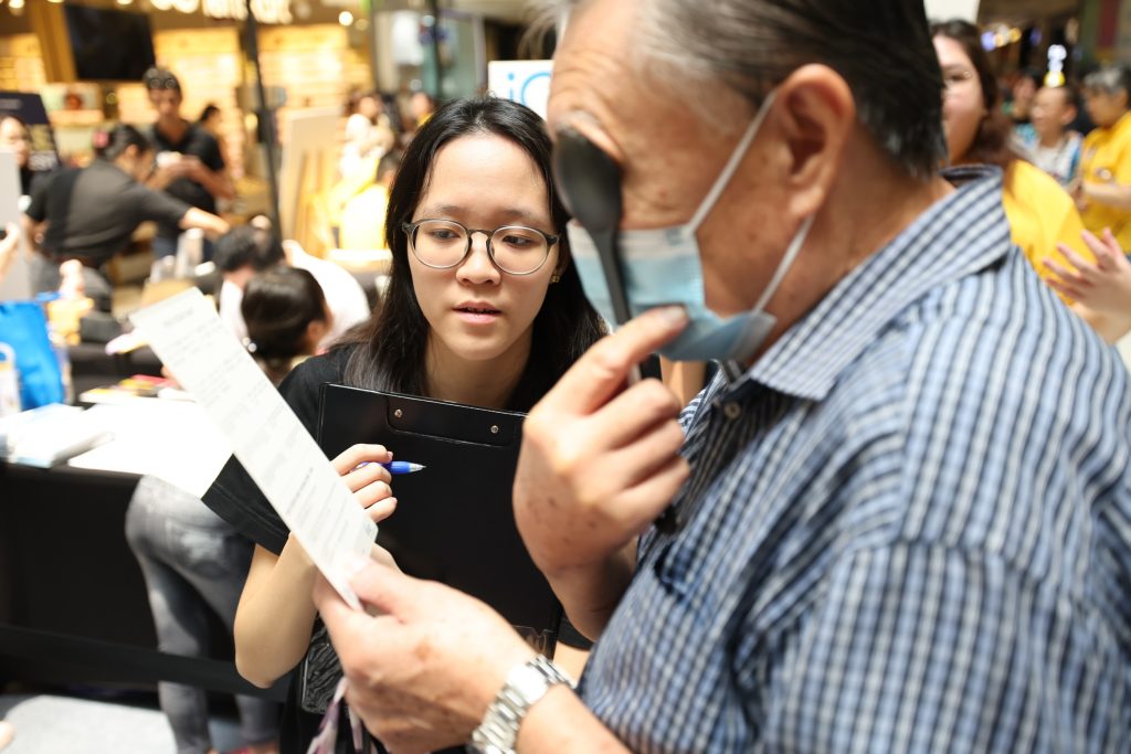 An elderly man holding an occluder over one eye while undergoing an eye test, focusing intently on the chart in front of him. 