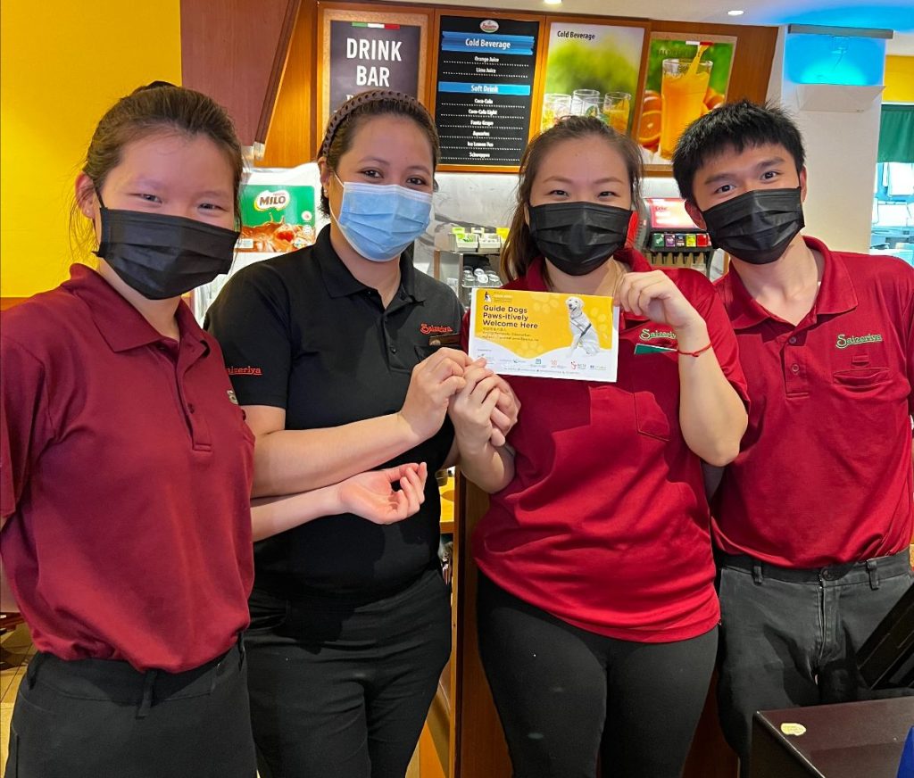 Four staff members from Saizeriya are posing for the camera while holding a “Guide Dogs Paw-sitivity Welcome Here” decal. Thank you Saizeriya for welcoming guide dogs.