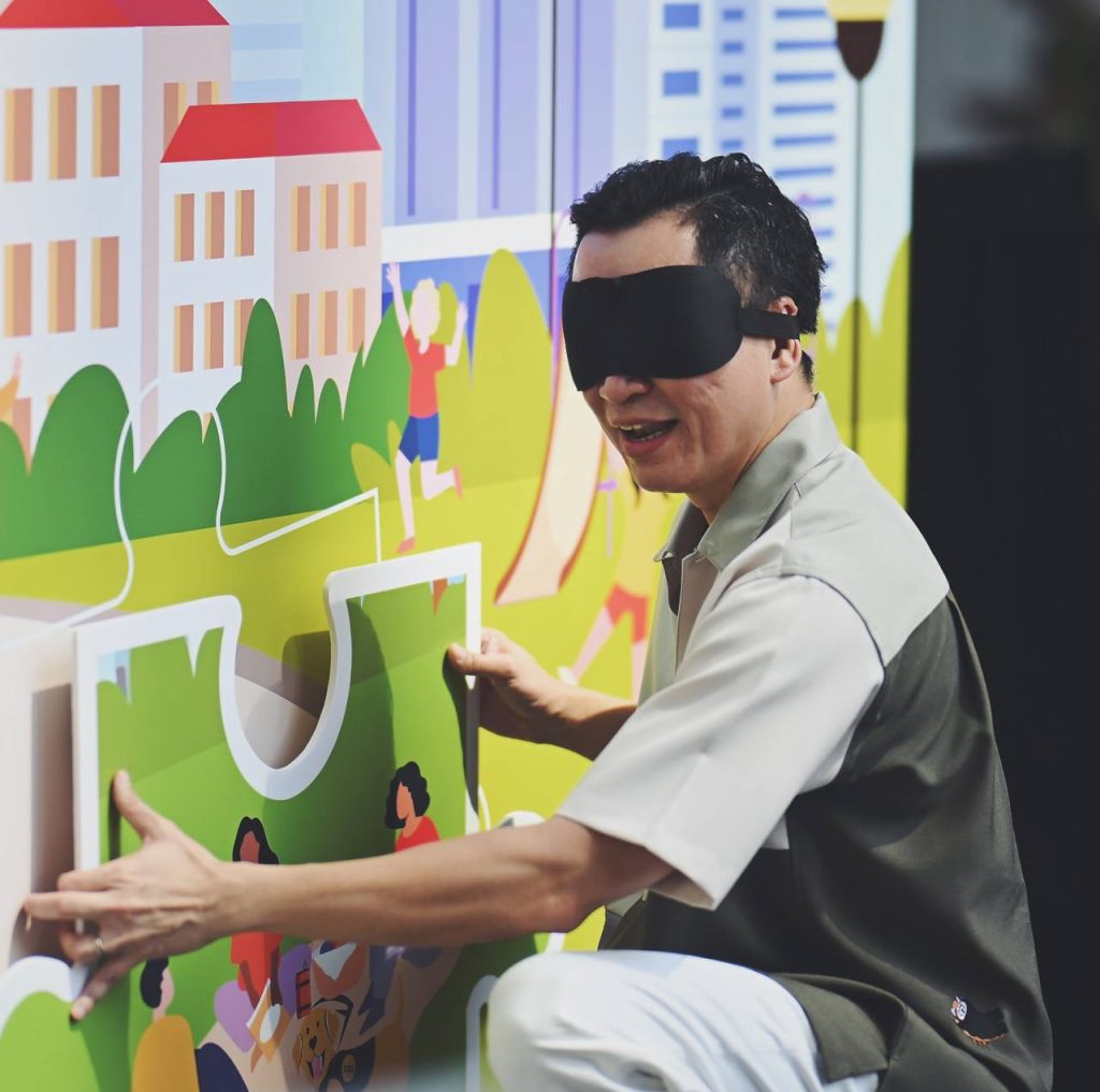 Mr. Eric Chua wears a blindfold while fitting a puzzle piece onto the stage backdrop.