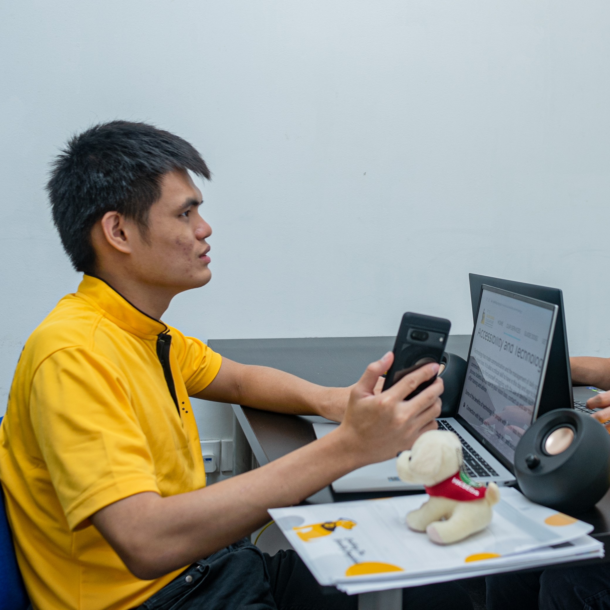 Guide dog user Hong Sen is using his laptop and phone while seated at a desk.