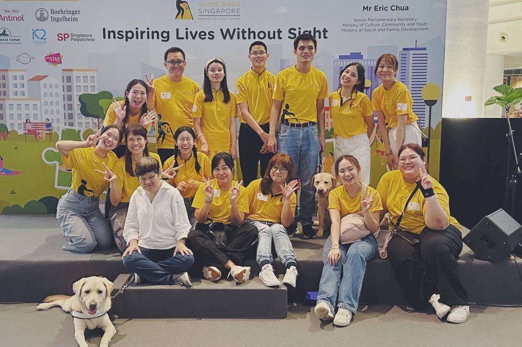 Group photo of GDS staff and clients smiling alongside two yellow Labrador guide dogs.