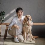Bessie sits with her right leg folded up, embracing her white guide dog, Jade, who is by her left side.