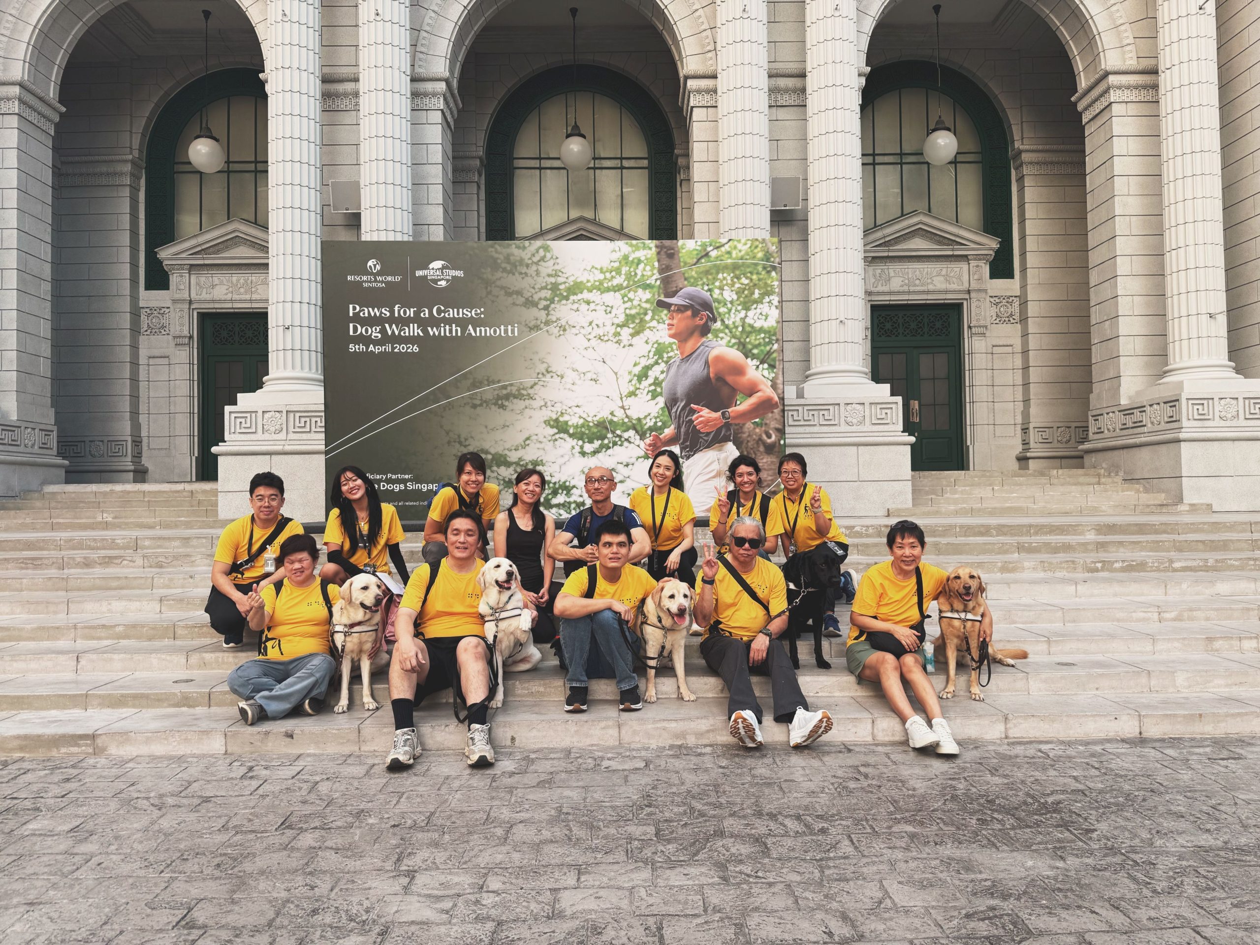 Guide Dog Singapore clients and staff pose in front of a banner at the Paws for a Cause: Dog Walk with Amotti