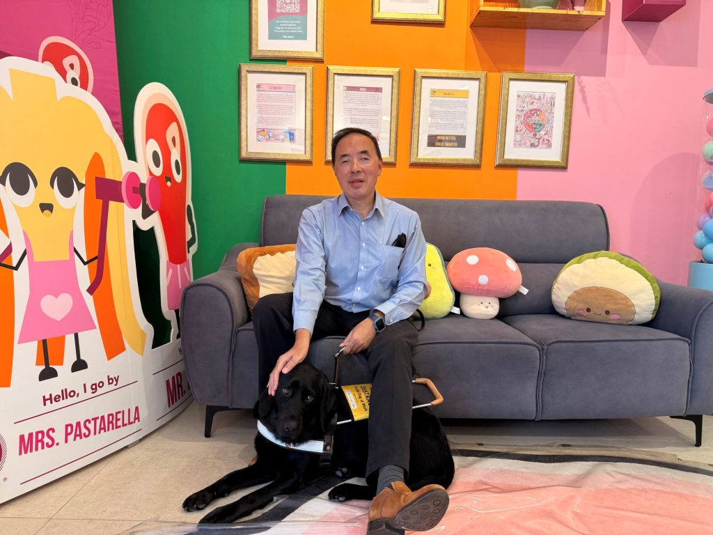 GDS client, Prof. Wong sits on a sofa chair with guide dog Leilah lying down under his leg
